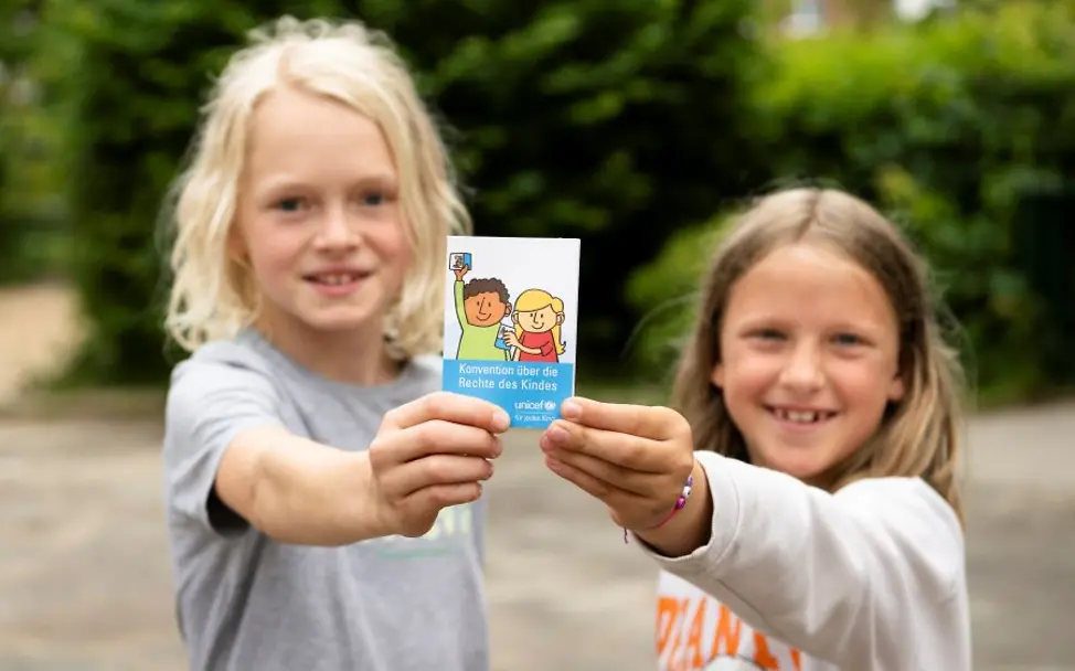 Zwei Kinder halten eine Broschüre zu Kinderrechten in die Kamera