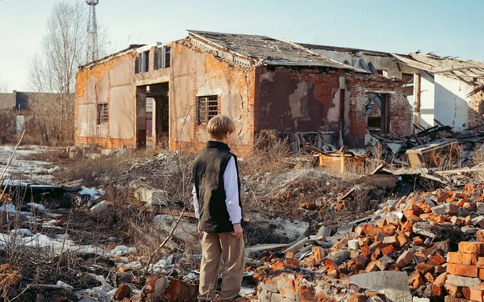 Schwere Kinderrechtsverletzungen: Roman (13) steht in der Ukraine vor einem zerstörten Gebäude