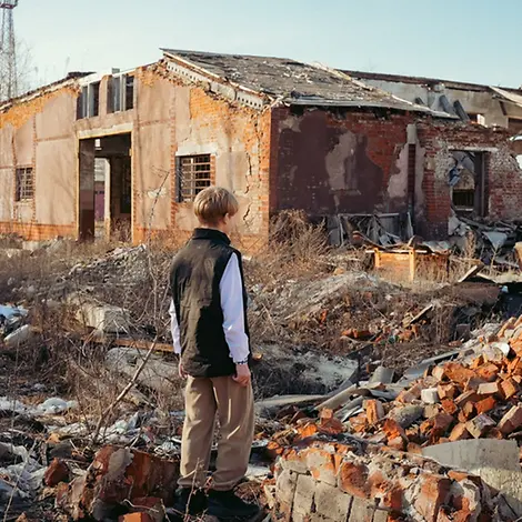 Schwere Kinderrechtsverletzungen: Roman (13) steht in der Ukraine vor einem zerstörten Gebäude
