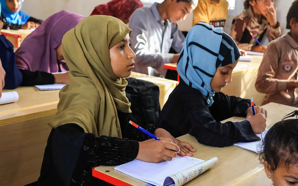 Bildung einfach erklärt: Ein Mädchen sitzt mit Schreibblock und Stift im Klassenzimmer.