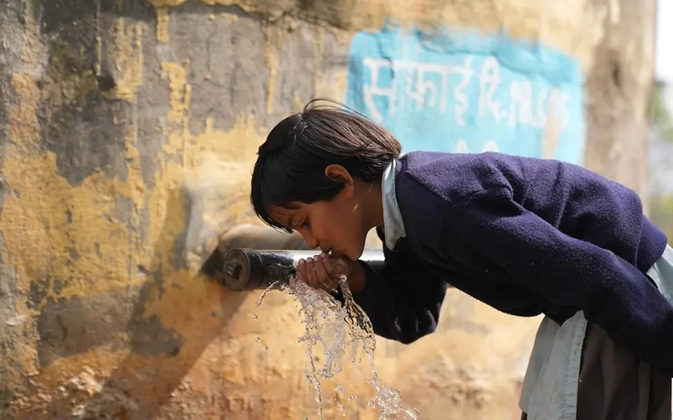 Dürre: Folgen für Kinder & Ursachen: Sara trinkt von einem Wasserhahn an ihrer Schule in Indien.