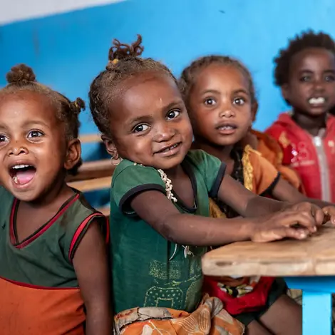 Wirkung im Klassenzimmer: Mehrere Kinder sitzen an Holzbänken und schauen in die Kamera