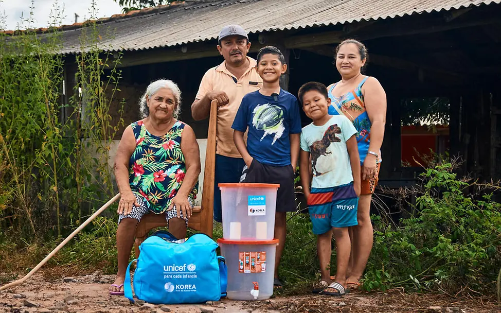 Waldbrand Folgen: Eine Familie steht mit UNICEF-Hilfsgütern vor ihrer Hütte.