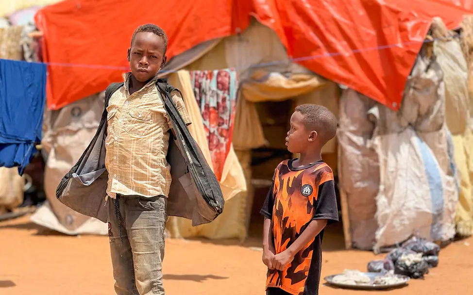Auf der Flucht vor Gewalt oder Dürre müssen viele Menschen alles zurücklassen, was sie besitzen. | © UNICEF SDGs einfach erklärt: Zwei Jungen stehen vor einem Zelt aus Planen im Flüchtlingslager.