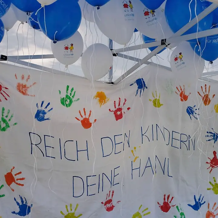 Auf einem Stoffbanner steht: "Reich den Kindern Deine Hand" mit vielen bunten Handabdrücken