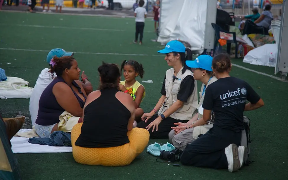 Humanitäre Hilfe: UNICEF-Mitarbeiter*innen sitzen neben einer Familie in einem Sportstadion