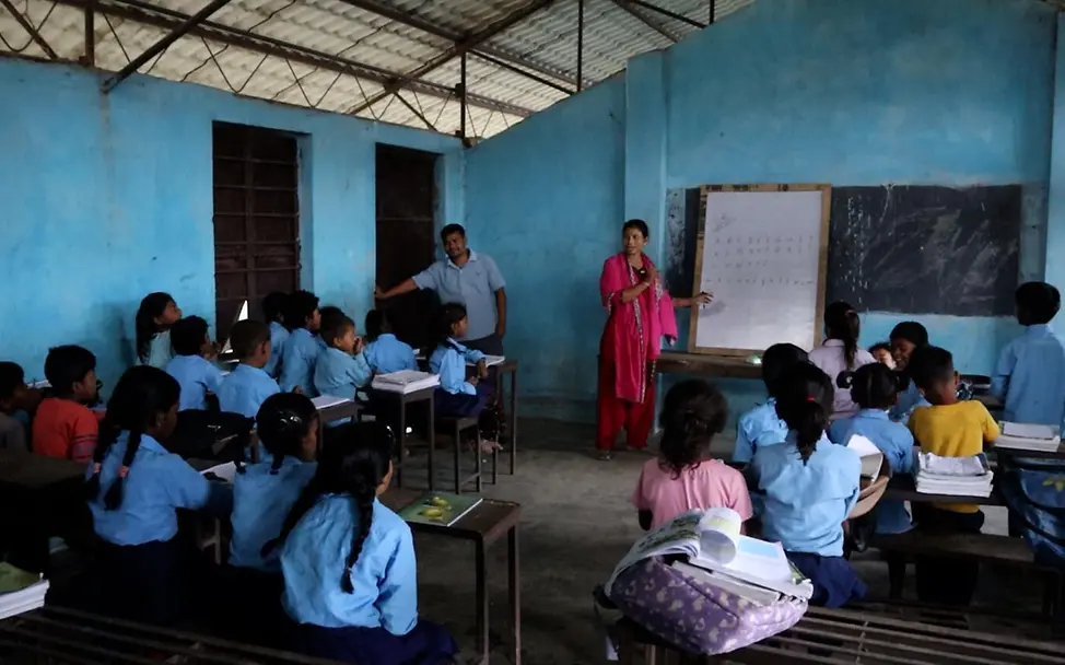 Armut oder ihre Lebensbedingungen zwingen viele Kinder in Nepal, die Schule frühzeitig abzubrechen. | © UNICEF/Schreiber Let Us Learn in Nepal: Schulkinder schauen in der Klasse auf die Tafel, während die Lehrerin erklärt.
