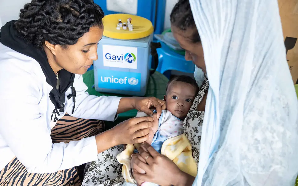 UNICEF versorgt Kinder in Krisengebieten mit Medikamenten und Impfungen. | © UNICEF/Bizuwerk Was ist Krieg einfach erklärt: Eine Gesundheitshelferin impft ein Baby auf dem Schoß seiner Mutter.