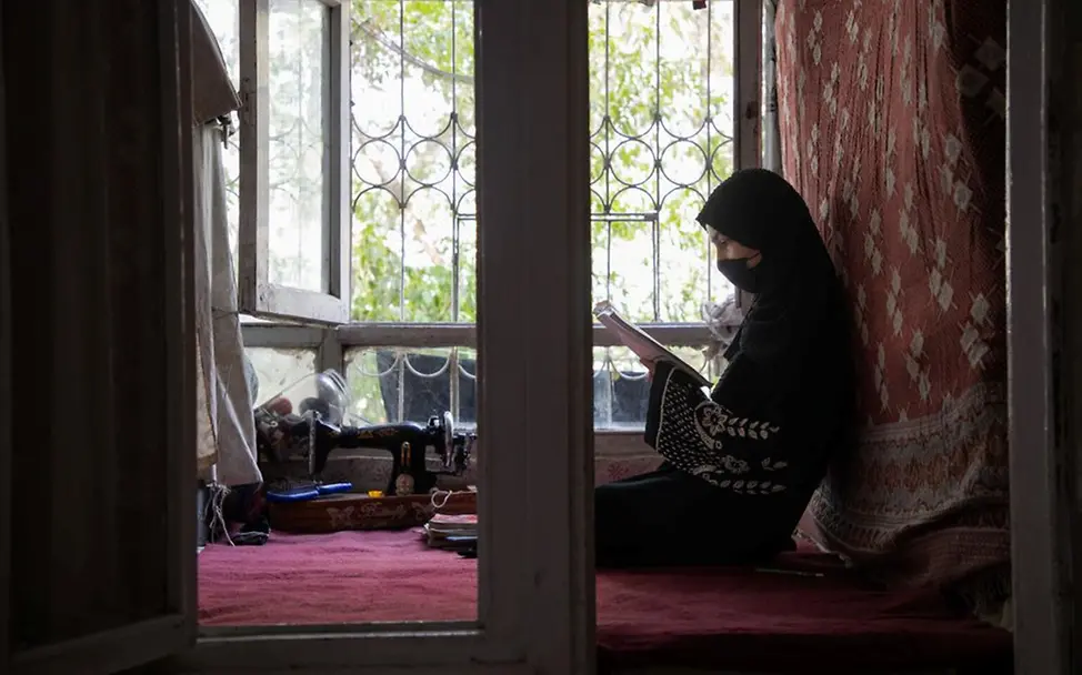 Ein Mädchen liest in einem Heft. | © UNICEF/Azizi Afghanistan Krise: Ein Mädchen sitzt in Afghanistan vor einem Fenster in einem Wohnraum. Sie liest in einem Heft.