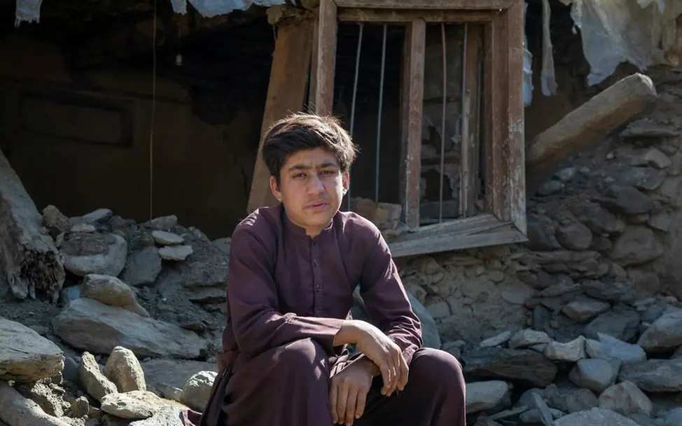Der 15-jährige Mohammad sitzt nach einem Erdbeben vor den Trümmern seines Hauses. | © UNICEF/Azizi Ein Junge sitzt dort auf Steinen und Blick in die Kamera, wo vor einem verheerenden Erdbeben das Wohnhaus der Familie stand.