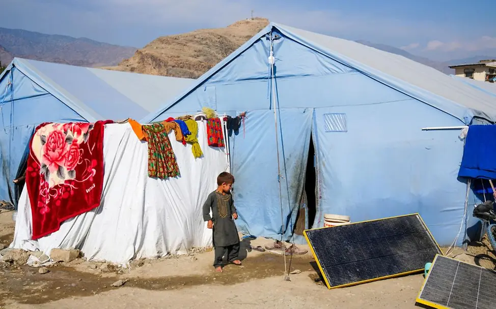 Der fünfjährige Rafi steht vor einem Zelt. Seine Familie hat nach einem Erdbeben alles verloren. | © UNICEF/Fazel Ein Junge steht vor einem hellblauen Zelt, das zu einer Notunterkunft für seine Familie geworden ist.