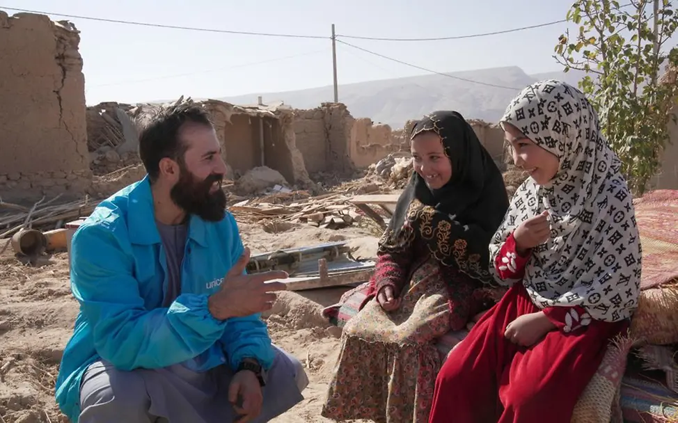 Ein UNICEF-Helfer spricht mit zwei Kindern, die wegen eines Erdbebens alles verloren haben. | © UNICEF/Karimi Afghanistan Krise: Nachdem ein Erdbeben Häuser zerstört hat, sitzt ein UNICEF-Helfer bei zwei Mädchen und spricht mit ihnen.
