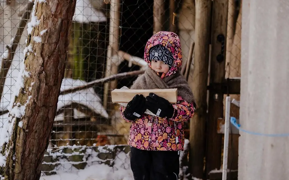 Kind trägt Feuerholz im Schnee in Ukraine | © UNICEF/UNI934307 Ukraine: Ein Kind steht im Schnee und trägt Winterkleidung; es hält Feuerholz mit Handschuhen.