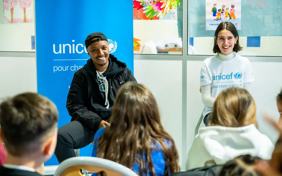 Austausch in Frankreich: UNICEF Vortrag vor Schulkindern | © UNICEF/Schneider Frankreich: Kinder hören zu, während zwei Personen neben einem UNICEF-Banner in einem Klassenraum sitzen.
