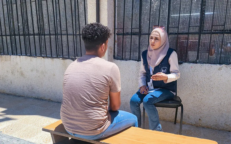Syrien: Individuelle Unterstützung im Schulumfeld | © UNICEF/Awad In Syrien spricht eine UNICEF-Fachkraft im Hof mit einem Jugendlichen und macht sich Notizen für die Unterstützung.