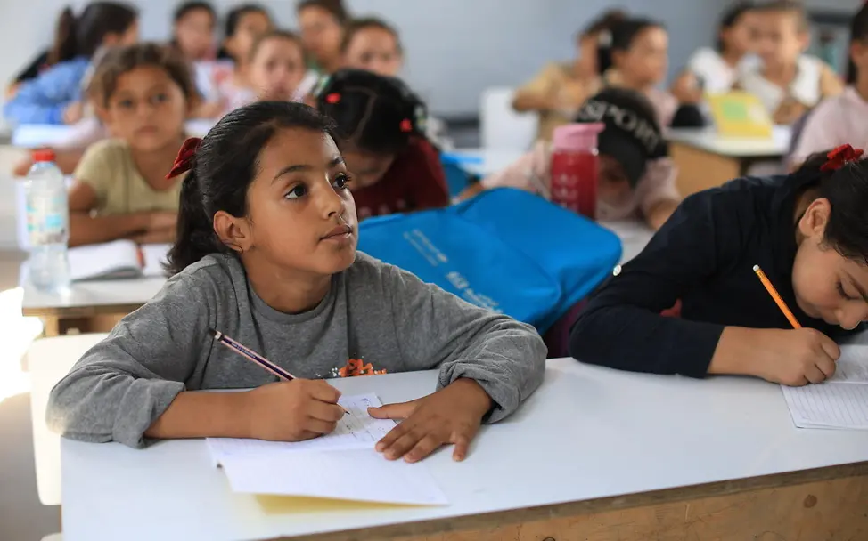 Gaza: Kinder lernen im Klassenraum | © UNICEF/UN0927764 In Gaza sehen Sie mehrere Kinder im Klassenraum; vorn hält ein Mädchen einen Stift und blickt aufmerksam nach vorn.