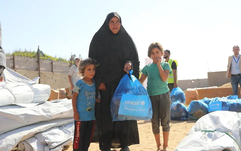 Eine Mutter steht mit ihren zwei Kindern in einer Notunterkunft. | © UNICEF Gaza: Eine Mutter steht mit ihren zwei Kindern in einer Notunterkunft.