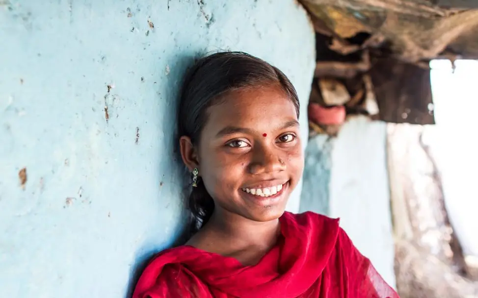 Die 14-jährige Vaishali lehnt lächelnd an einer blauen Wand. 