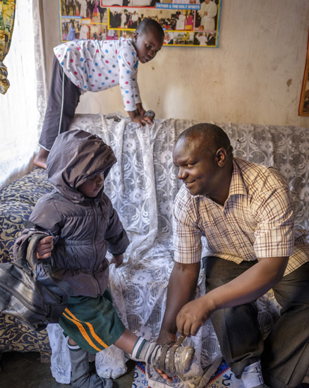 moses mit seinen beiden Töchtern Pretty und Abigail | © UNICEF/Ose Uganda: Ein Vater hilft seiner Tochter beim Schuhe ausziehen