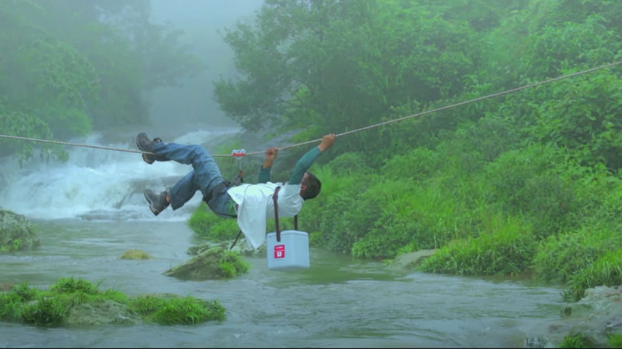Indien: Ein Träger klettert an einem Seil über einen Fluss