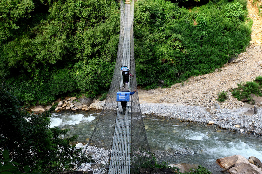 Nepal: Zwei Träger überqueren einen Fluss über eine Brücke