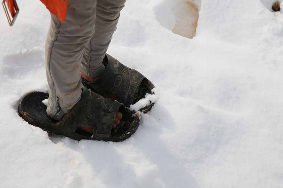 Ein Flüchtlingskind steht in viel zu großen Sandalen im Schnee.