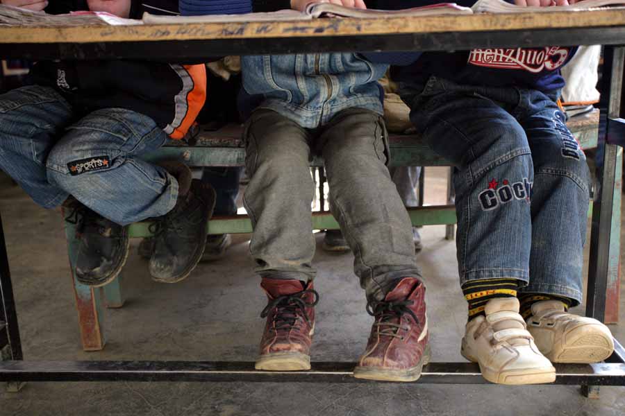 Albanien: Die Beine von drei Jungen, die sich in der Schule einen Tisch teilen.