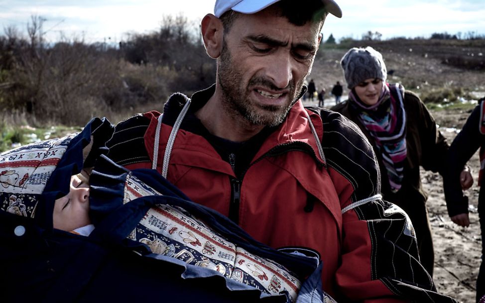 Jamal Majati trägt seinen Sohn Youssef über ein matschiges Feld in Mazedonien.