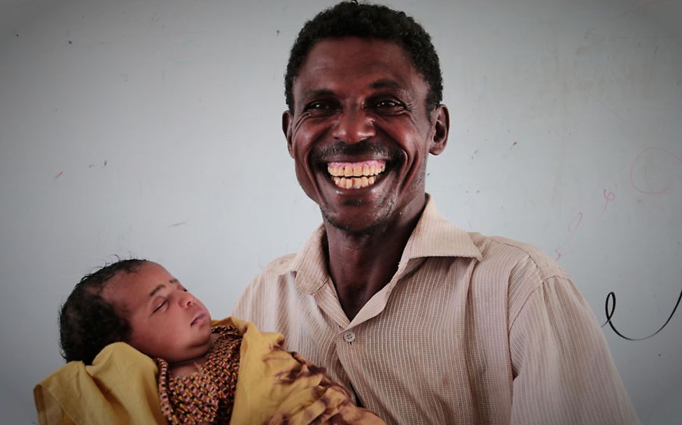 Ein Vater hält sein Baby im Arm – überglücklich, dass es überlebt hat und weitgehend wohlauf ist.