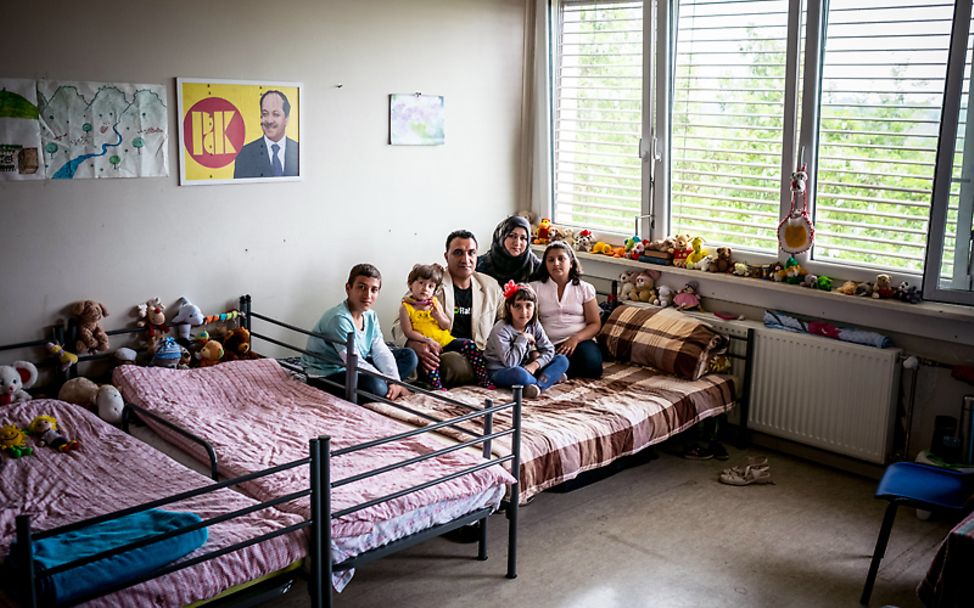 Bericht Flüchtlingskinder: Die Familie sitzt zusammen auf einem Bett in einer Flüchtlingskunterkunft