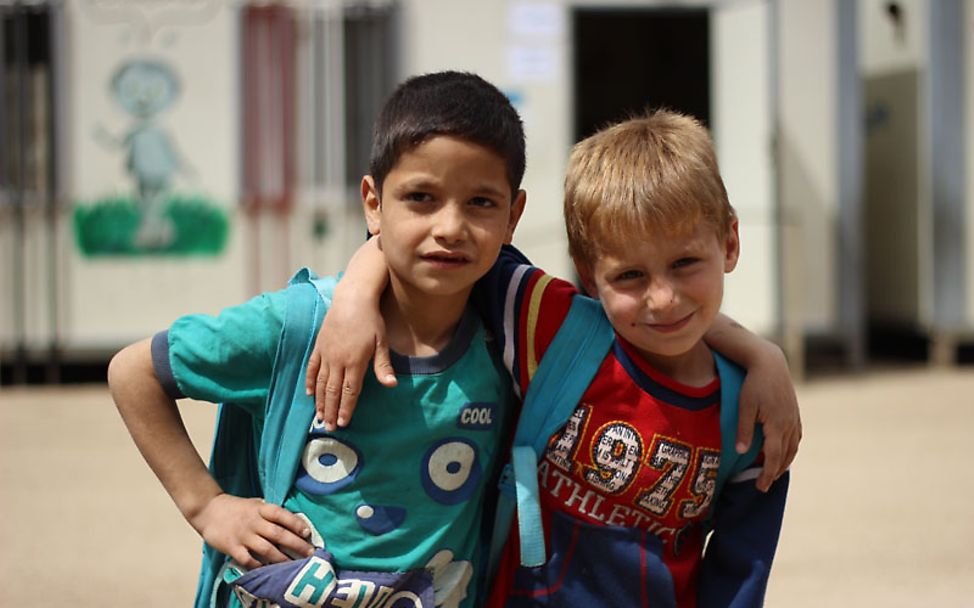 Zwei kleine Jungen stehen Arm in Arm vor ihrer mit Hilfe von UNICEF aufgebauten Schule.