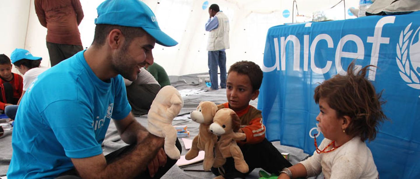 Minderjährige Geflüchtete: Ein UNICEF-Helfer spielt mit zwei Flüchtlingskindern.  