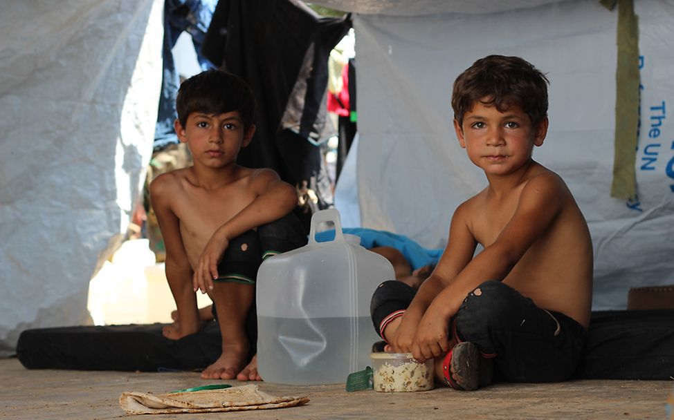 Zwei syrische Jungen sitzen neben einem Wasserkanister in einem provisorischen Zelt in Aleppo.