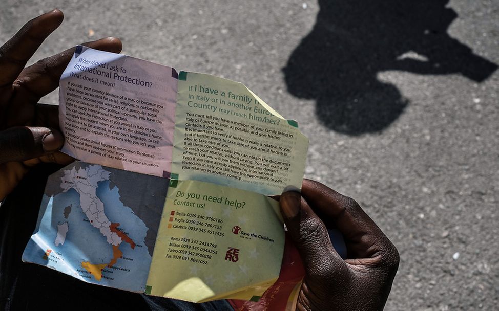 Ein Junge schaut auf ein Infopapier für Flüchtlinge in Sizilien. 