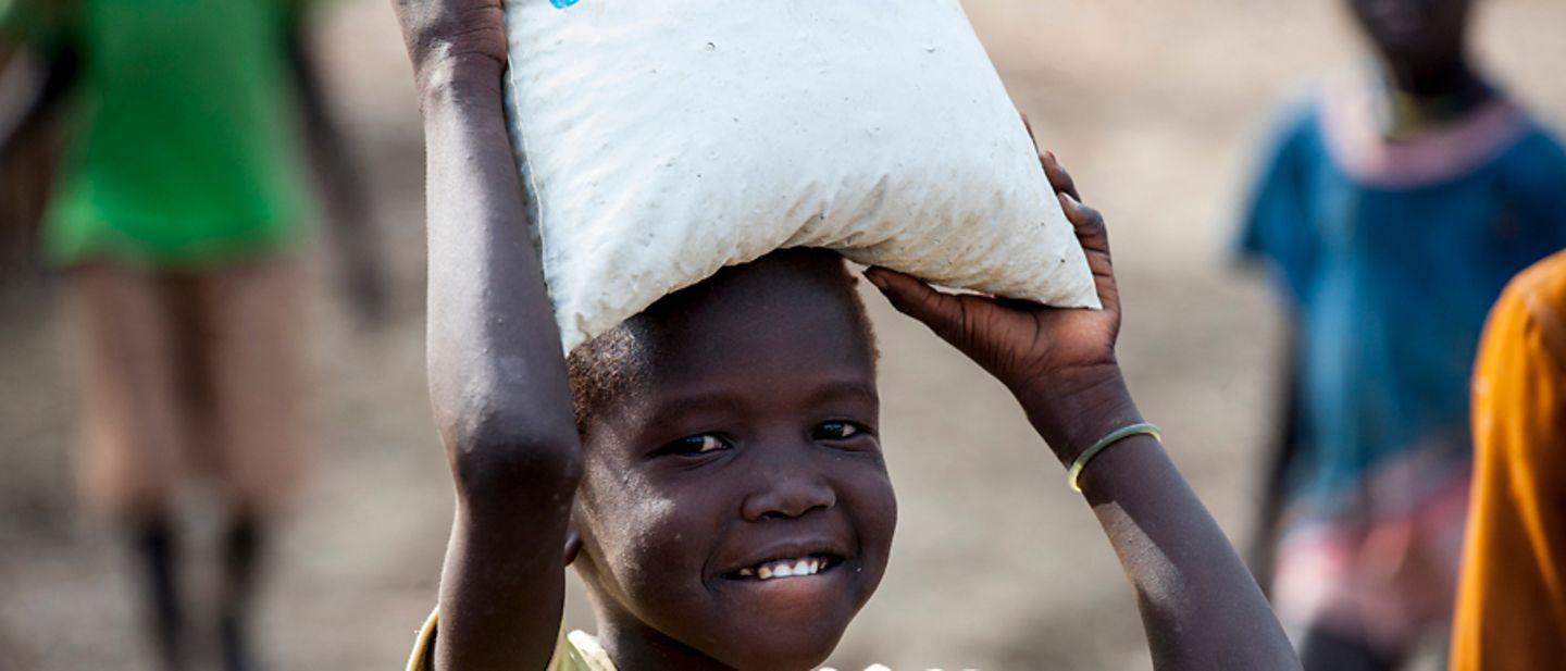 Südsudan: Ein Mädchen trägt einen Beutel mit UNICEF-Hilfsgütern auf dem Kopf