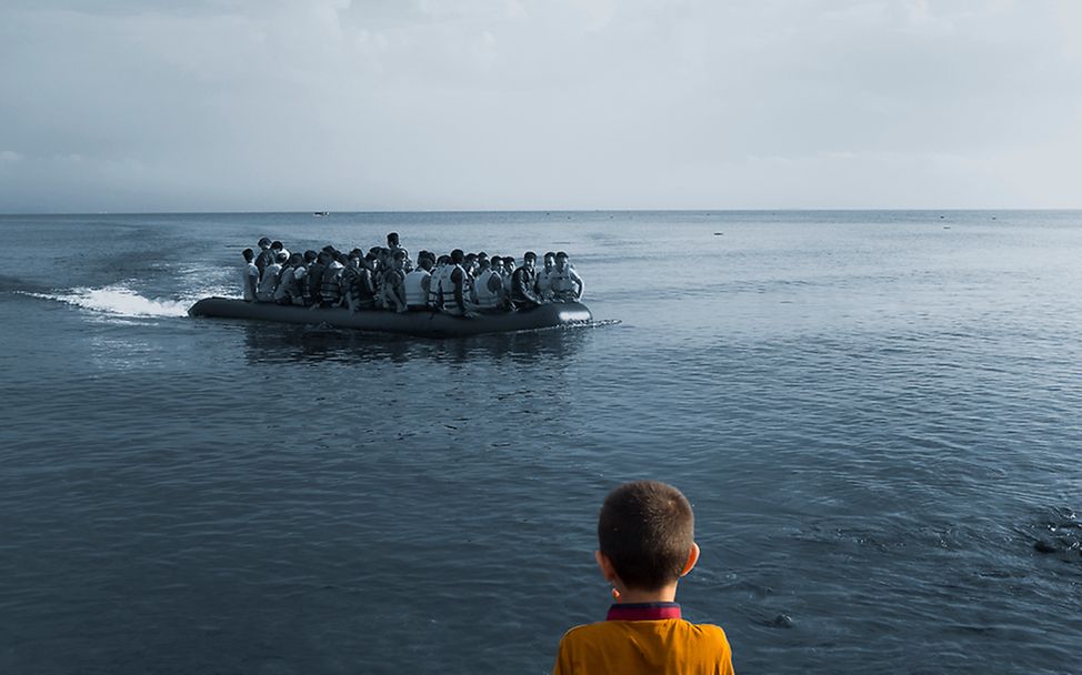 Ein Junge blickt auf das Meer in Lesbos, Griechenland hinaus, wo gerade ein Boot mit Flüchtlingen ankommt.