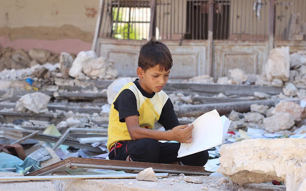 Nothilfe Syrien: Junge mit Heft inmitten von Trümmern