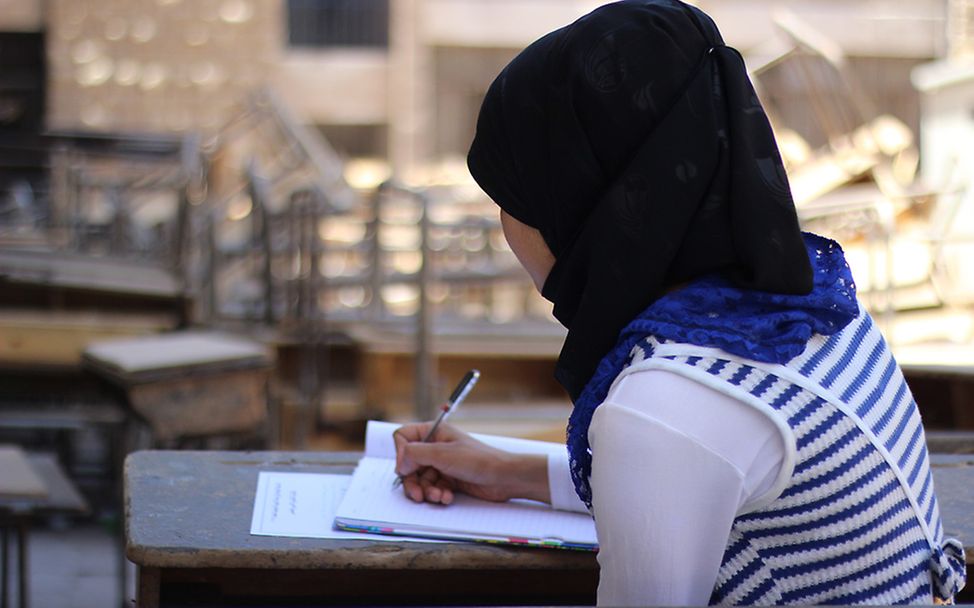 Abitur in Syrien: Rama sitzt an einem Schreibtisch und lernt für ihre Prüfungen. Ihr Gesicht ist zu ihrem Schutz nicht zu sehen.