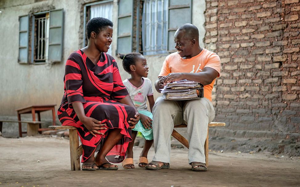 Uganda: Die siebenjährige Vera sitzt mit ihren Eltern auf einer Bank