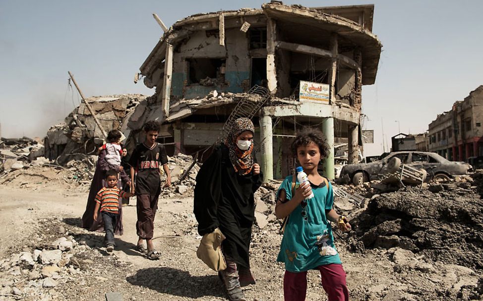 Frauen und Kinder in Mossul passieren zerstörte Häuser auf der Suche nach Schutz und Sicherheit.