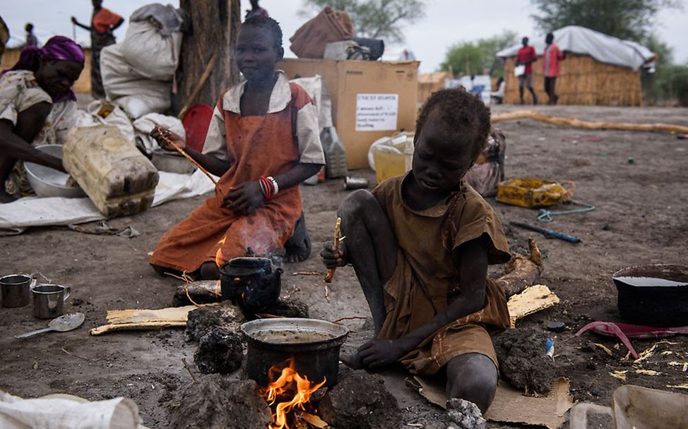 Südsudan: Ein Kind sitzt neben einem Kochtopf am Feuer