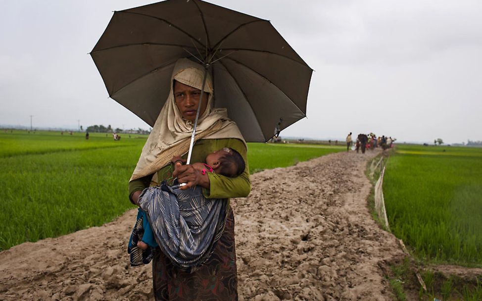 Eine Mutter trägt ihr Kind im Regen durch Reisfelder