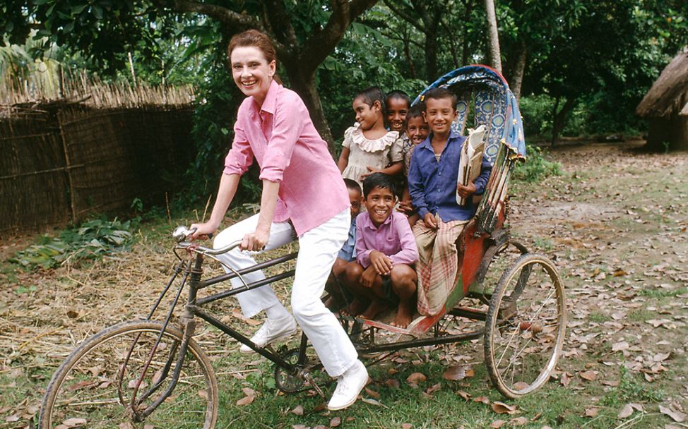 Bangladesch: UNICEF-Botschafterin Audrey Hepburn fährt Kinder in einem Fahrrad spazieren 
