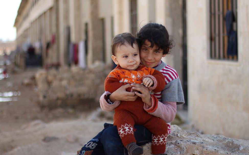 Syrien Krieg: Ein Kind in Aleppo hält ein Baby in seinen Armen