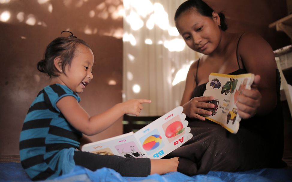Belize: Tyra sitzt auf einem Bett und lernt das Alphabet
