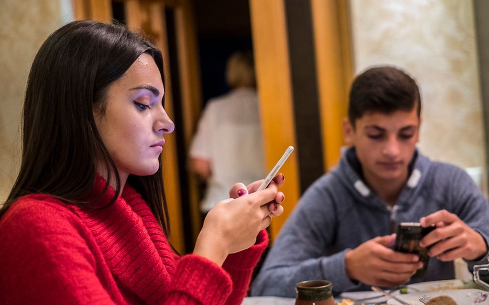 Zwei Jugendliche sitzen beim Abendessen an ihren Smartphones.