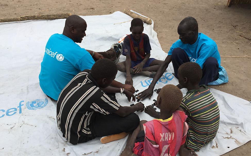 Südsudan: Michael sitzt mit einem Ball auf einer Plane und spricht mit Kindern