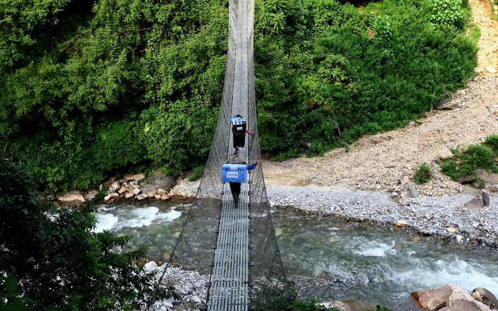 Nepal: Zwei Träger überqueren einen Fluss über eine Brücke