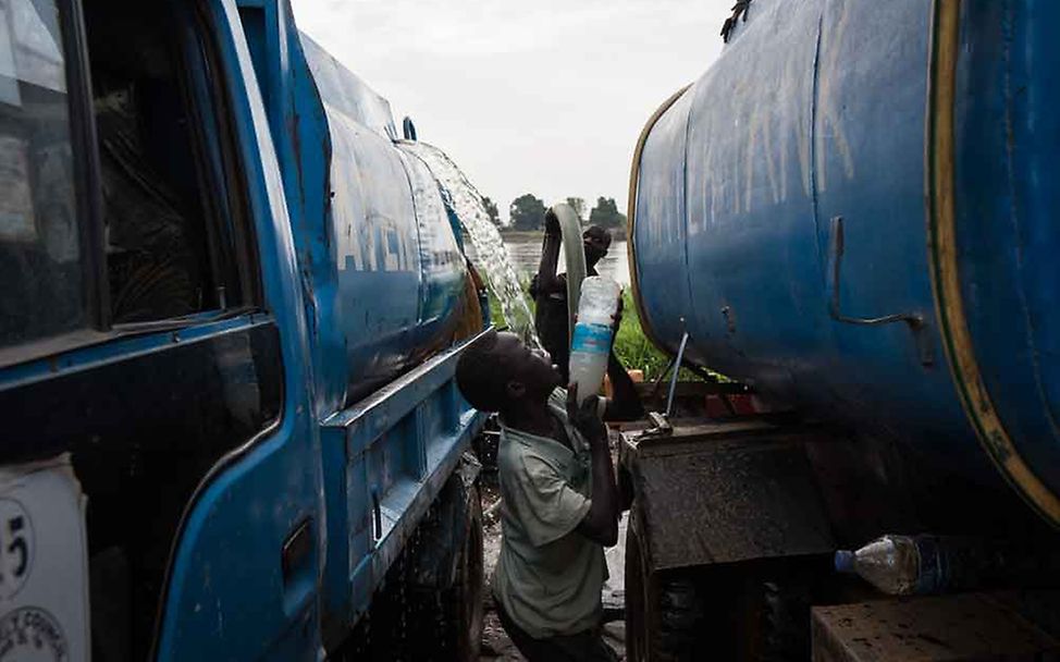 Francis wirft eine Flasche mit Chlorlösung zu einem Truck rüber. | © UNICEF/Hatcher-Moore  
