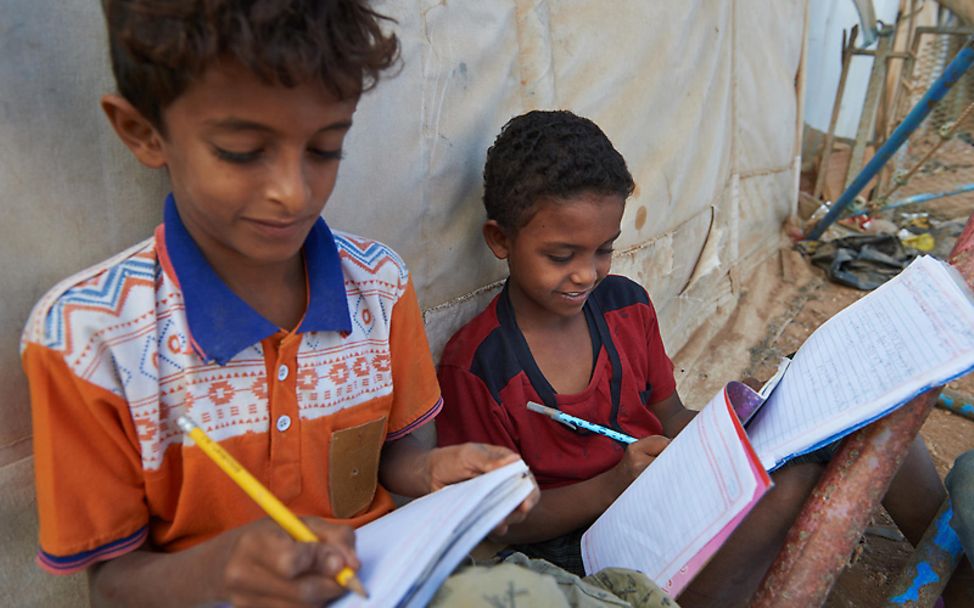 Camp Djibouti: zwei Jungen schreiben in ihre Schulhefte.